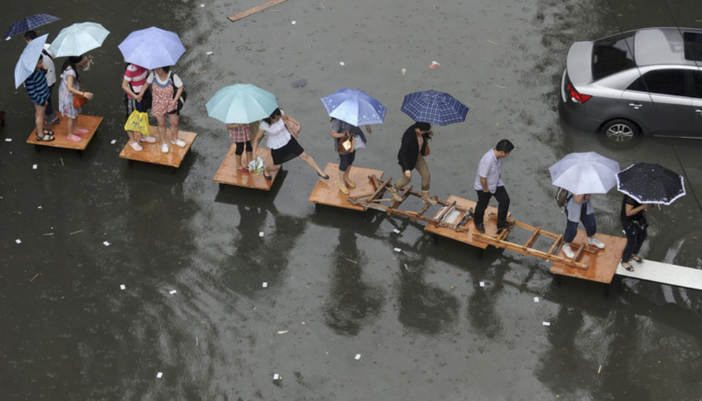 People hold umbrellas as they cross a flooded street by stepping on wooden tables and ladders amid heavy rainfalls in Wuhan